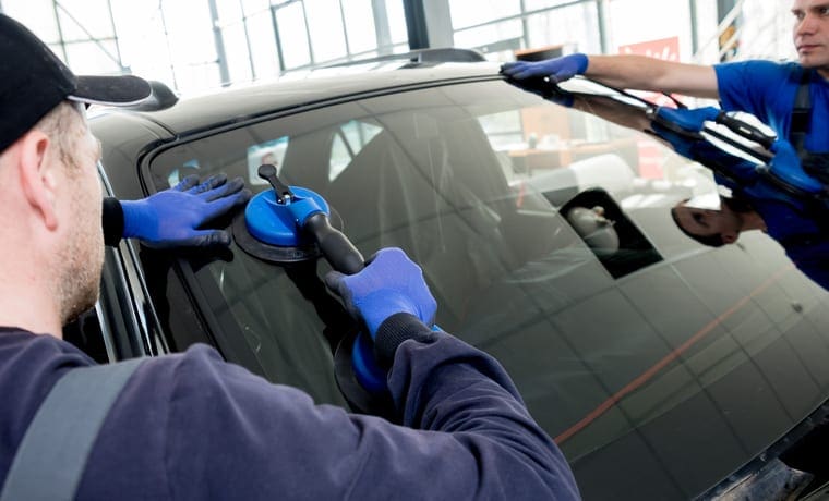 Automobile special workers replacing windscreen or windshield of a car in auto service station garage.